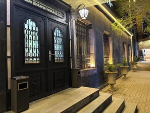 Une entrée noire, richement décorée, avec des grilles en métal, un banc en pierre et un chemin pavé menant à un bâtiment.