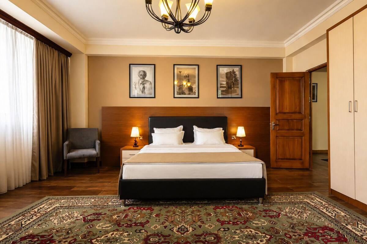 Habitación de hotel con una cama grande, dos mesitas de noche con lámparas, una silla, alfombra estampada y un candelabro.