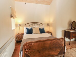 A bedroom with a wooden bed, two bedside tables with lamps, a dresser, and a window with blinds. - THE COACH HOUSE COTTAGE, pet friendly, with open fire in Ballycommon (NENAGH)