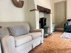 A living room with a beige sofa, a green armchair, a green stove, and a white door. - THE COACH HOUSE COTTAGE, pet friendly, with open fire in Ballycommon (NENAGH)