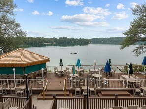 Eine Terrasse mit Sitzgelegenheiten mit Blick auf einen See, ein Gebäude mit Strohdach und ein Boot in der Ferne.