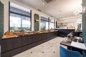 Una larga mesa buffet con diversos alimentos, una lámpara de araña y vistas a través de amplios ventanales.