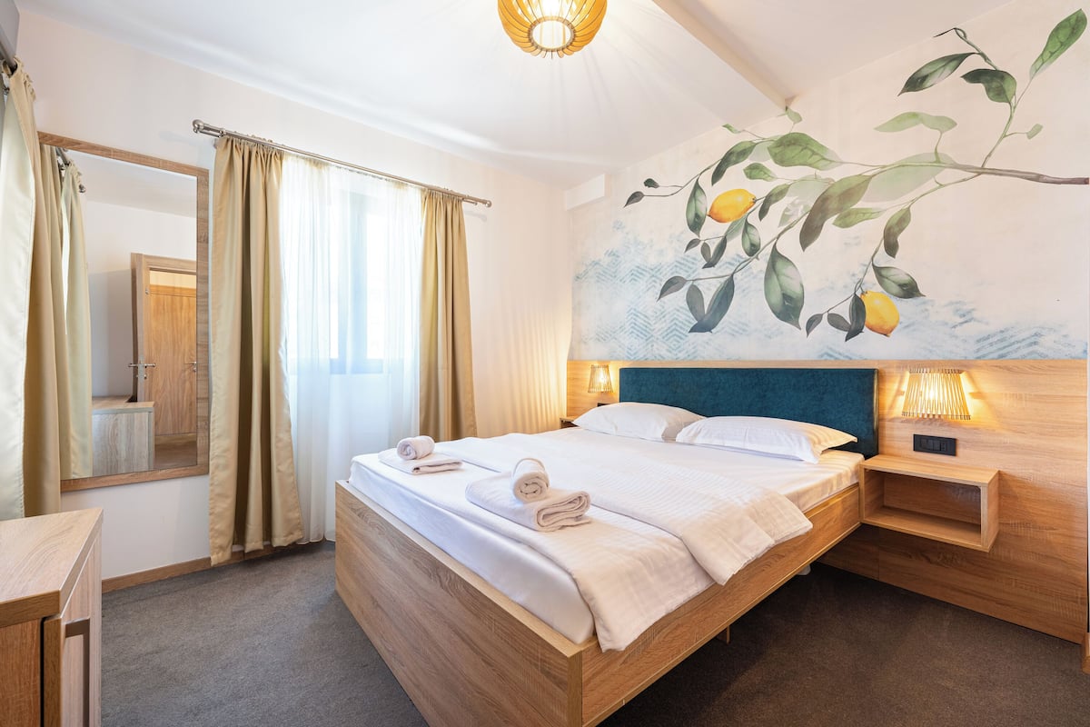 Una habitación de hotel con una cama grande, un cabecero de madera, una mesita de noche, un espejo y un cuadro en la pared.