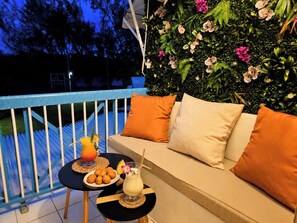 A balcony with a sofa, cushions, a table with drinks and snacks, and a lush green wall. - Tropical Chic Studio with Views of the Marina and Pool - Le Carayou Residence🌴 (Les Trois-Îlets)