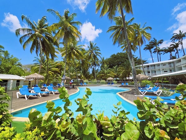 A poolside area with lounge chairs, palm trees, and a building in the background. - Tropical Chic Studio with Views of the Marina and Pool - Le Carayou Residence🌴 (Les Trois-Îlets)