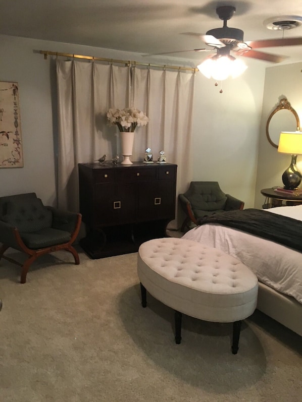 Un dormitorio con cama, dos sillones, cómoda, ventilador de techo y lámpara.