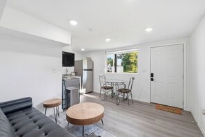 A modern living room with a sofa, round wooden table, and a dining area with chairs.