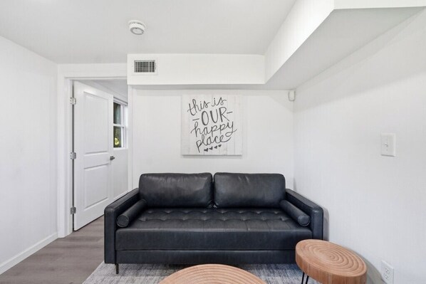 A modern living room with a black leather sofa, a wooden stool, and a motivational wall art piece.
