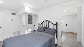 Quarto com cama, paredes brancas, uma porta e um interruptor de luz.