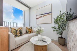 Ein modernes Wohnzimmer mit einer Couch, einem runden Couchtisch, einer Blumenvase, einem Bild an der Wand und einer Zimmerpflanze.