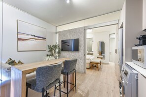 Een moderne keuken met een houten tafel, twee barkrukken, een flatscreen televisie en een wasmachine.