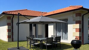 En uteplats med ett bord och stolar, en grill och en byggnad med ett rött tegeltak.