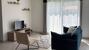 Ett modernt vardagsrum med en platt-TV, en soffa, en fåtölj, ett litet bord och dekorativa hyllor.