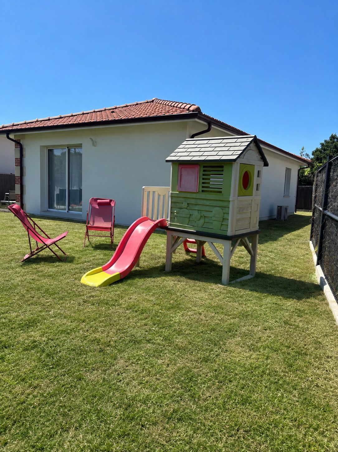 Une cabane de jeu avec un toboggan et une petite chaise longue dans un jardin.