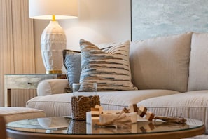 Una sala de estar moderna con un sofá, una mesa de centro de vidrio y almohadones decorativos.