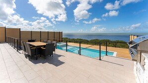 Une terrasse sur le toit avec une piscine, du mobilier d’extérieur et une vue sur l’océan.