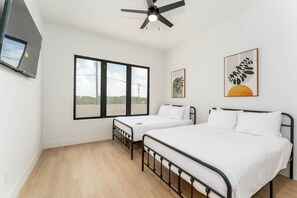 A bedroom with two beds, a ceiling fan, large windows, and artwork on the walls. - 4,000 SF Waterfront Home w/ Pool, Sleeps 22 (Port Isabel)