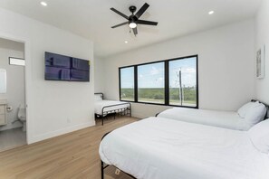 Ein modernes Schlafzimmer mit Bett, einem kleinen Tisch, Deckenventilator, Fenster mit Blick und einem Gemälde an der Wand.