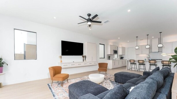 Un salon moderne comprenant un canapé, deux fauteuils, une table basse, un téléviseur et un ventilateur de plafond.