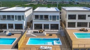 Un bâtiment moderne doté de trois piscines distinctes, chacune ayant une terrasse en bois et des chaises longues.