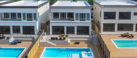 A modern building with three separate swimming pools, each with a wooden deck and lounge chairs.