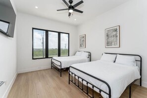 Une chambre avec deux lits, un ventilateur de plafond, de grandes fenêtres et des œuvres d’art accrochées aux murs.