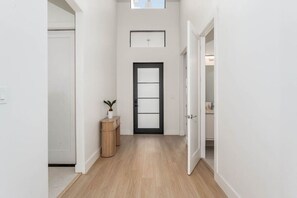 Un couloir avec un plancher en bois, une porte dotée d’un cadre noir, une petite plante posée sur une console en bois et un interrupteur sur le mur.