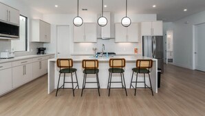 Une cuisine moderne avec des meubles blancs, un îlot central doté de tabourets et des luminaires suspendus.