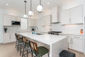 A modern kitchen with a central island, bar stools, a microwave, and a stove. - 4,000 SF Waterfront Home w/ Pool, Sleeps 22 (Port Isabel)