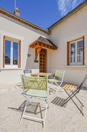 A patio with a table and chairs, a wooden door, and a small garden area. - Vacation Rental in the Seine Valley (LA MOTTE TILLY)