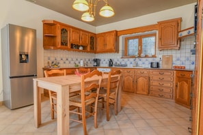 A kitchen with wooden cabinets, a stainless steel refrigerator, a dining table with chairs, and a window.