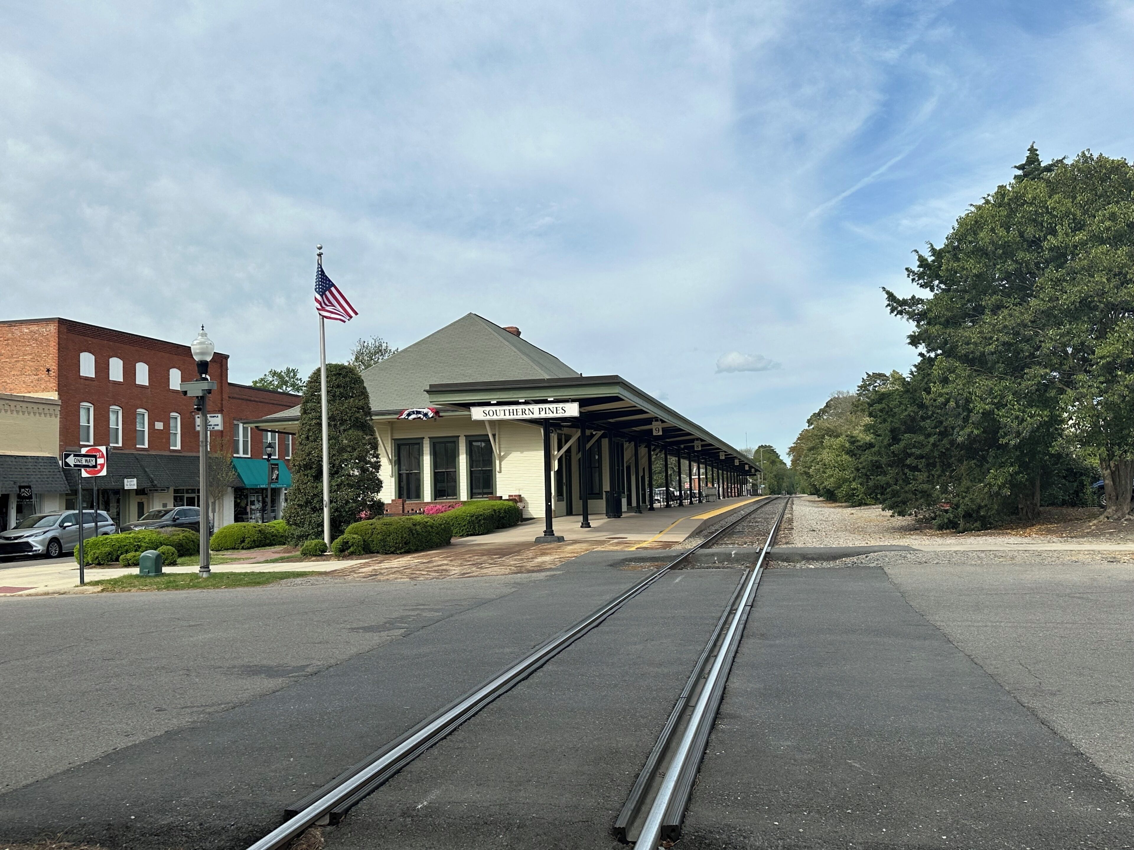 Una estación de tren con un andén cubierto, un edificio de ladrillo y una bandera estadounidense.