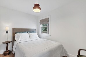 Une chambre à coucher comprenant un lit, une table de chevet, une lampe, une fenêtre avec vue et un luminaire suspendu.