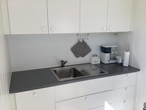 A kitchen with a stainless steel sink, a coffee maker, and a kettle. There are two hanging kitchen towels and a box labeled 'SNAPS'. - 4 Person Holiday Home in Stromstad (Stromstad)