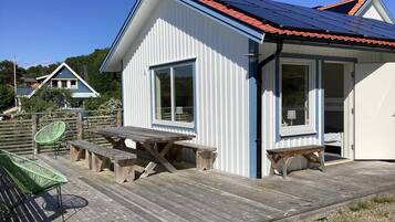 A white building with a red roof, a wooden deck with picnic tables, and a green chair.