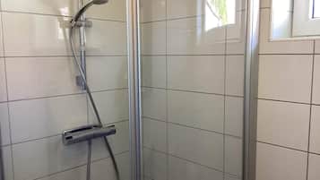 A shower area with a glass door, a handheld showerhead, and a handheld shower attachment.