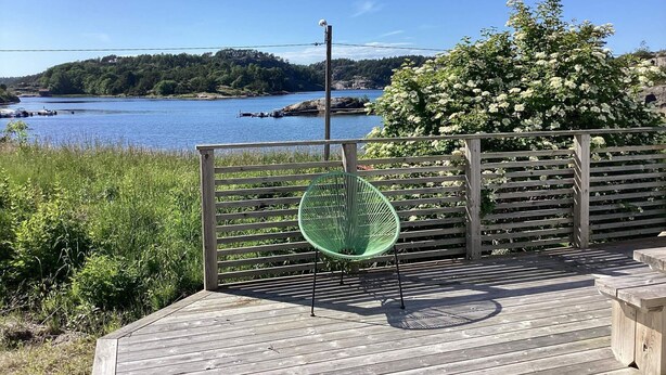 A wooden deck with a green chair, overlooking a body of water and a forested hill. - 4 Person Holiday Home in Stromstad (Stromstad)