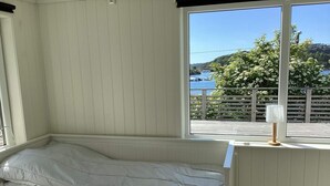 A room with a bed, a window with a view of a body of water and greenery, and a lamp on the windowsill. - 4 Person Holiday Home in Stromstad (Stromstad)