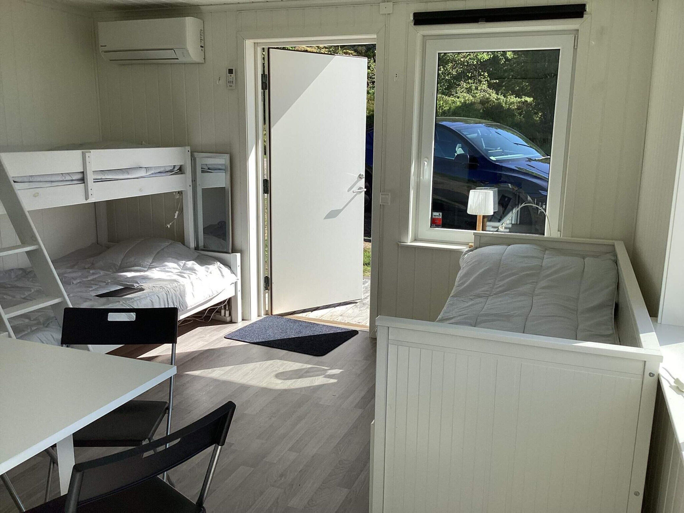 A compact room with bunk beds, a table, chairs, a window with a view of a car, and an air conditioning unit.
