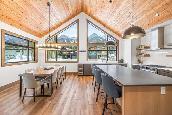A modern kitchen with a large island, wooden ceiling, and large windows offering mountain views.