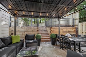 Eine überdachte Terrasse mit Gartenmöbeln, einer Treppe und einem Holzzaun.