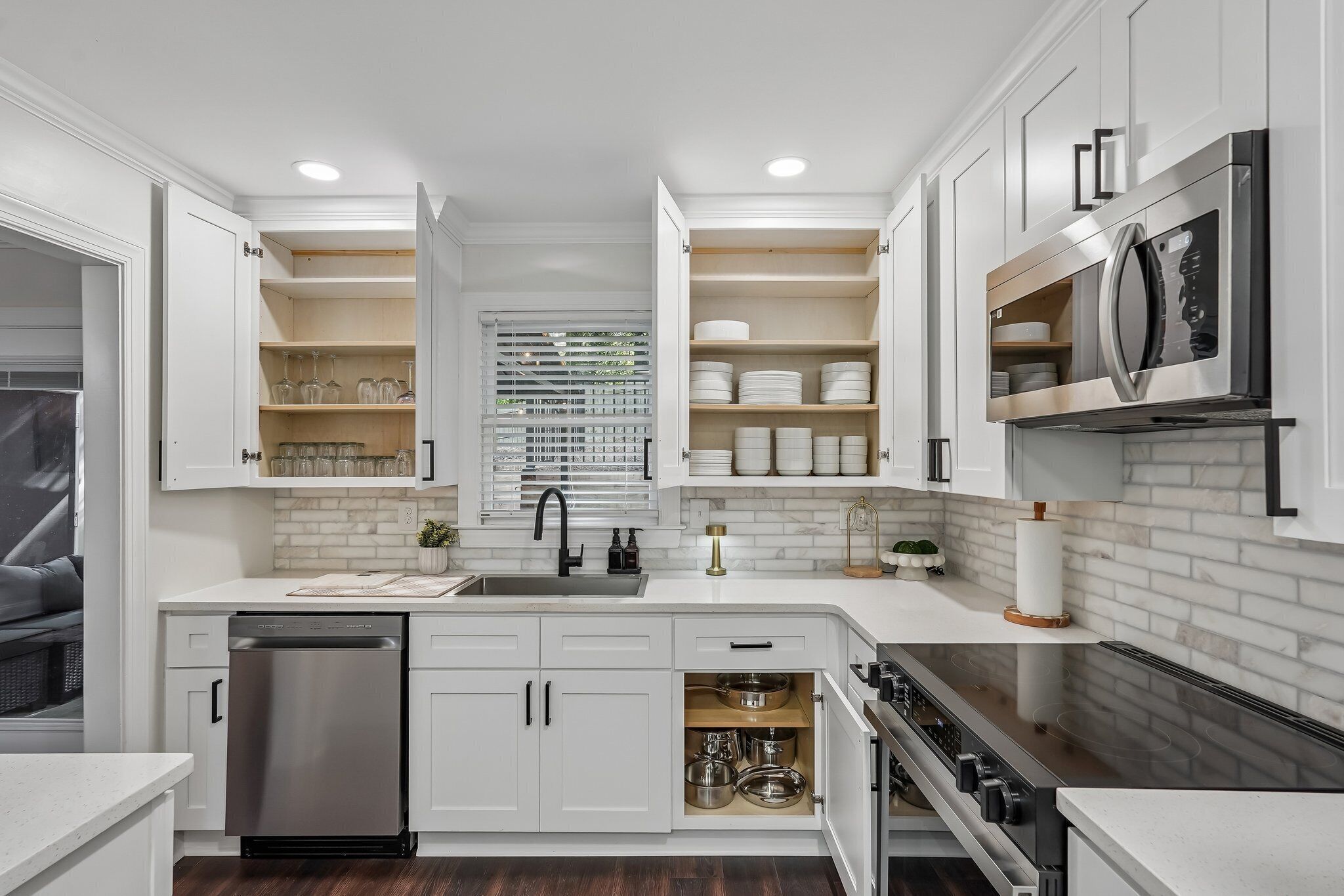 A modern kitchen with white cabinetry, a stainless steel dishwasher, a built-in oven, and a microwave.
