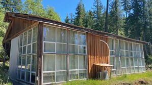 A wooden cabin with large windows, a wooden deck, and a gravel path.