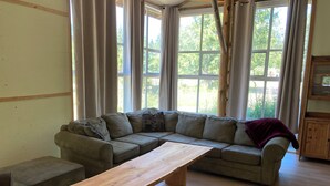 A living room with a sectional sofa, a wooden coffee table, and large windows with curtains.