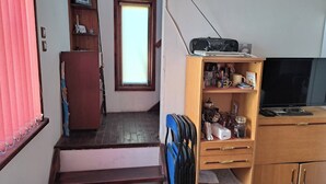 Ein Zimmer mit einem Holztisch, einem Stuhl, einem Fernseher, einem Bücherregal und einem Fenster.