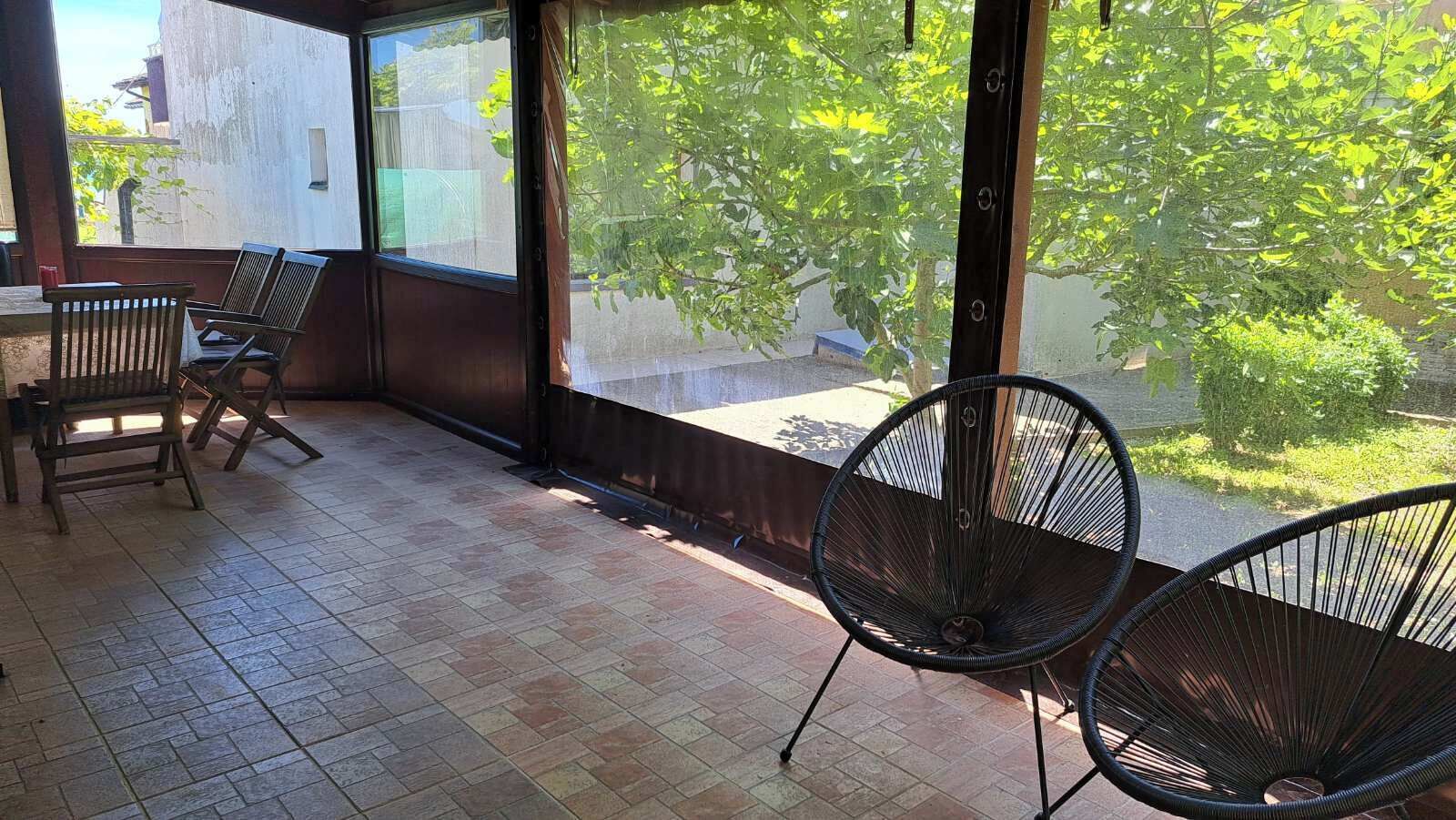 En udendørs patio med fliset gulv, to træstole og en sort metalstol.