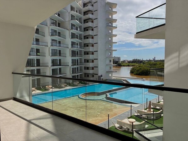 Ein Wohngebäude mit Pool auf dem Dach, Glasbrüstung und Blick auf einen Fluss und Grünflächen.
