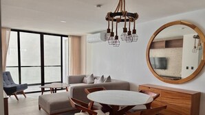 Un salon moderne avec un canapé, une table de salle à manger ronde entourée de chaises, un meuble en bois et un grand miroir accroché au mur.