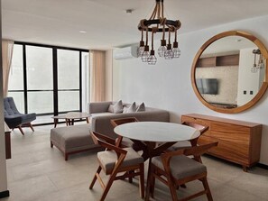 Ein modernes Wohnzimmer mit einer Couch, einem runden Esstisch mit Stühlen, einer Holzkommode und einem großen Spiegel an der Wand.