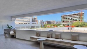 Un espace extérieur moderne aménagé avec un canapé et deux tables rondes, offrant une vue sur le paysage urbain, avec ses bâtiments et ses chantiers de construction.